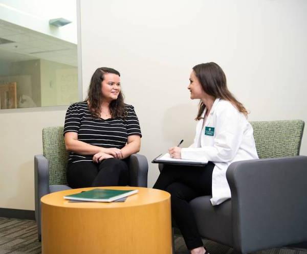 A nurse speaking with a patient while writing information on her tablet.